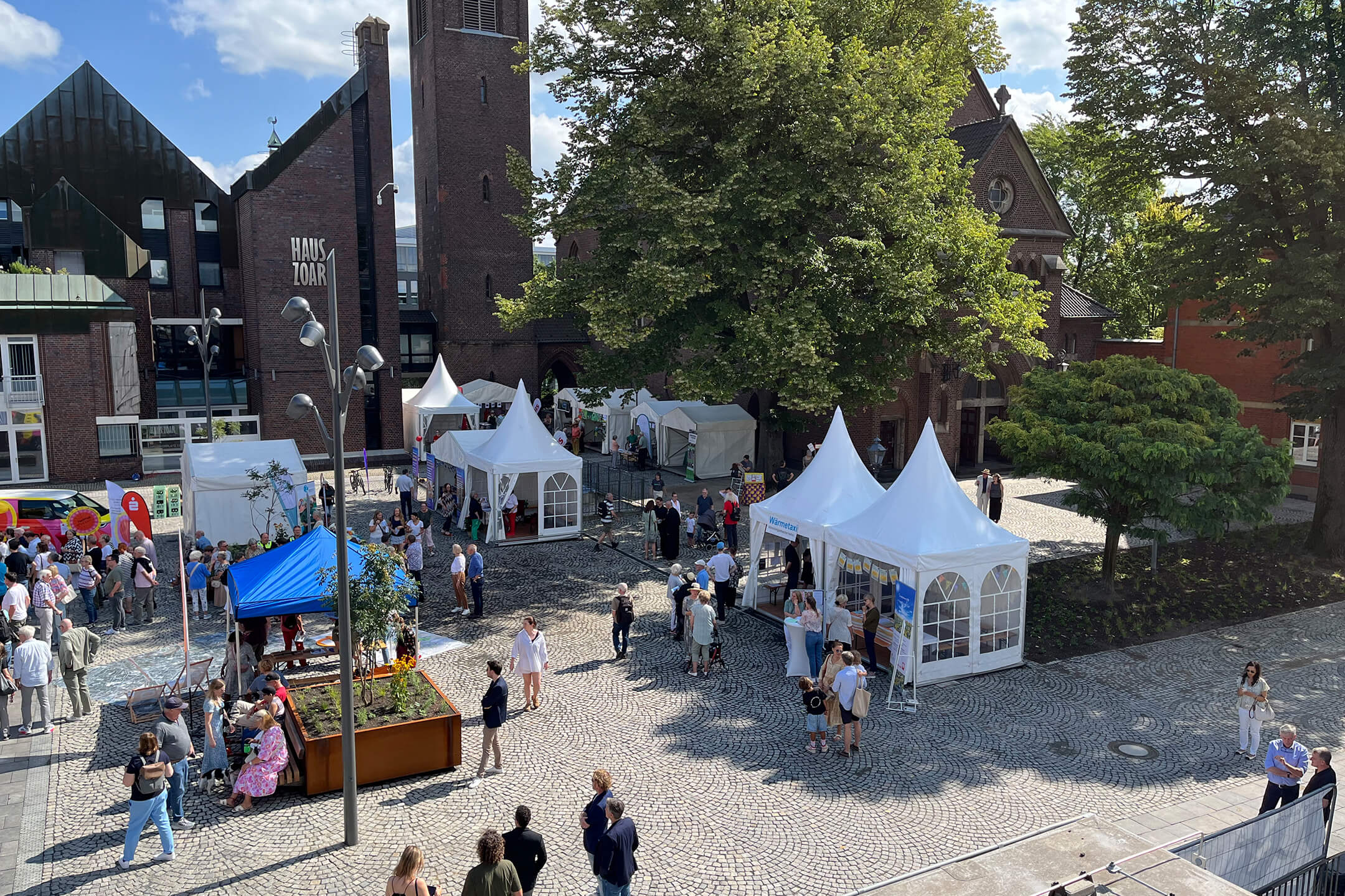 Viele Menschen versammeln sich, bei gutem Wetter, um die aufgebauten Zelte und Pavillons des „Markt der Möglichkeiten“ bei der Wiedereröffnung des Kapuzinerplatzes, vor der Markthalle.