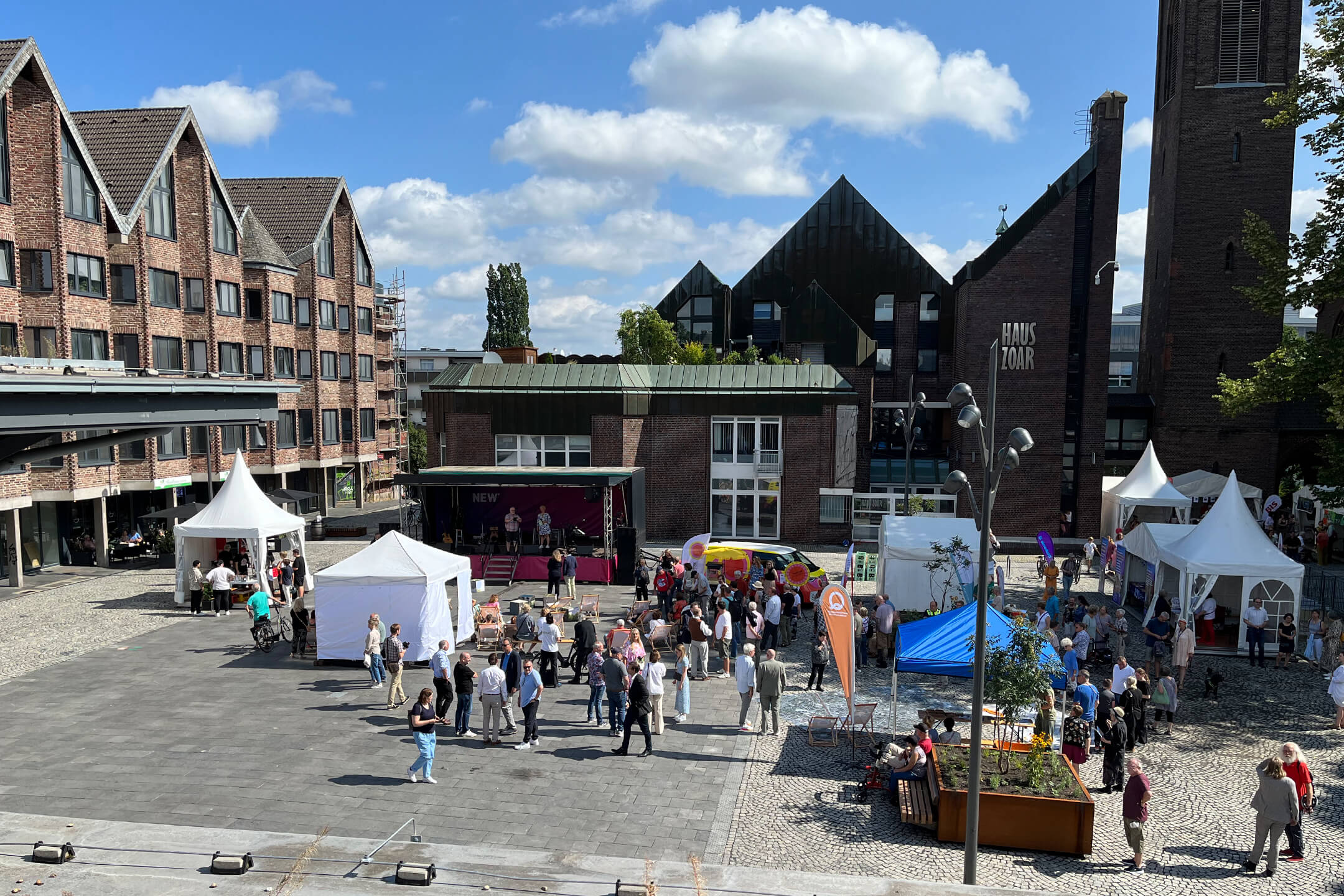 Bei gutem Wetter steht eine große Gruppe von Menschen versammelt um aufgebaute Zelte und Pavillons auf dem neu eröffneten Kapuzinerplatz.