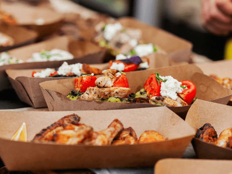 Nahaufnahme mehrerer, nachhaltiger Street Food Schalen, z.B. gefüllt mit Chicken Wings, Salat mit gebratenen Hähnchenstreifen etc. 